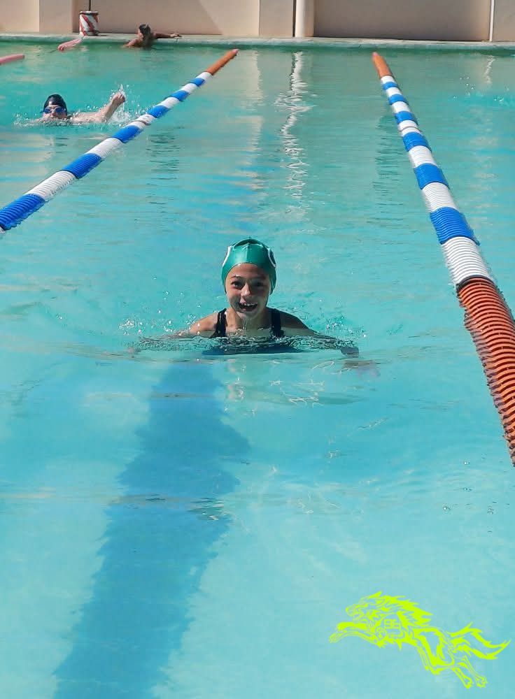 Grace swimming breaststroke in a lap pool during training, wearing a teal swimming cap and goggles, with lane dividers visible